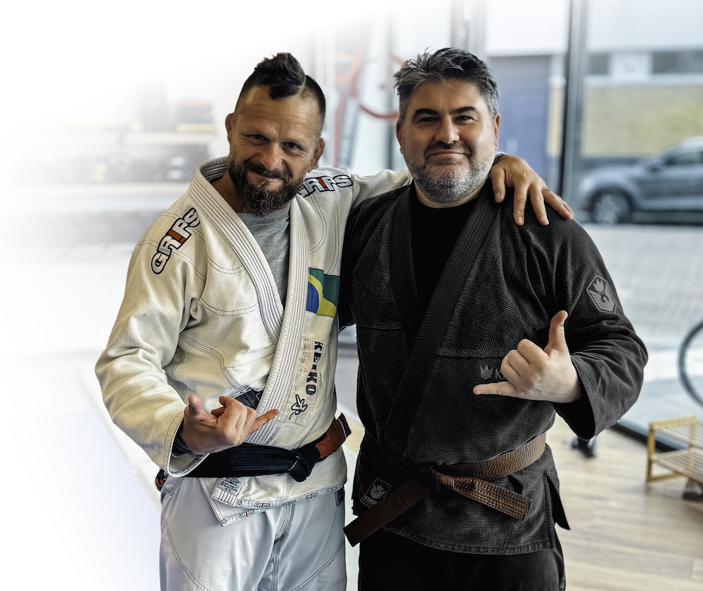 Two men pose together on the mat after a BJJ brown belt promotion, smiling with pride in their uniforms.