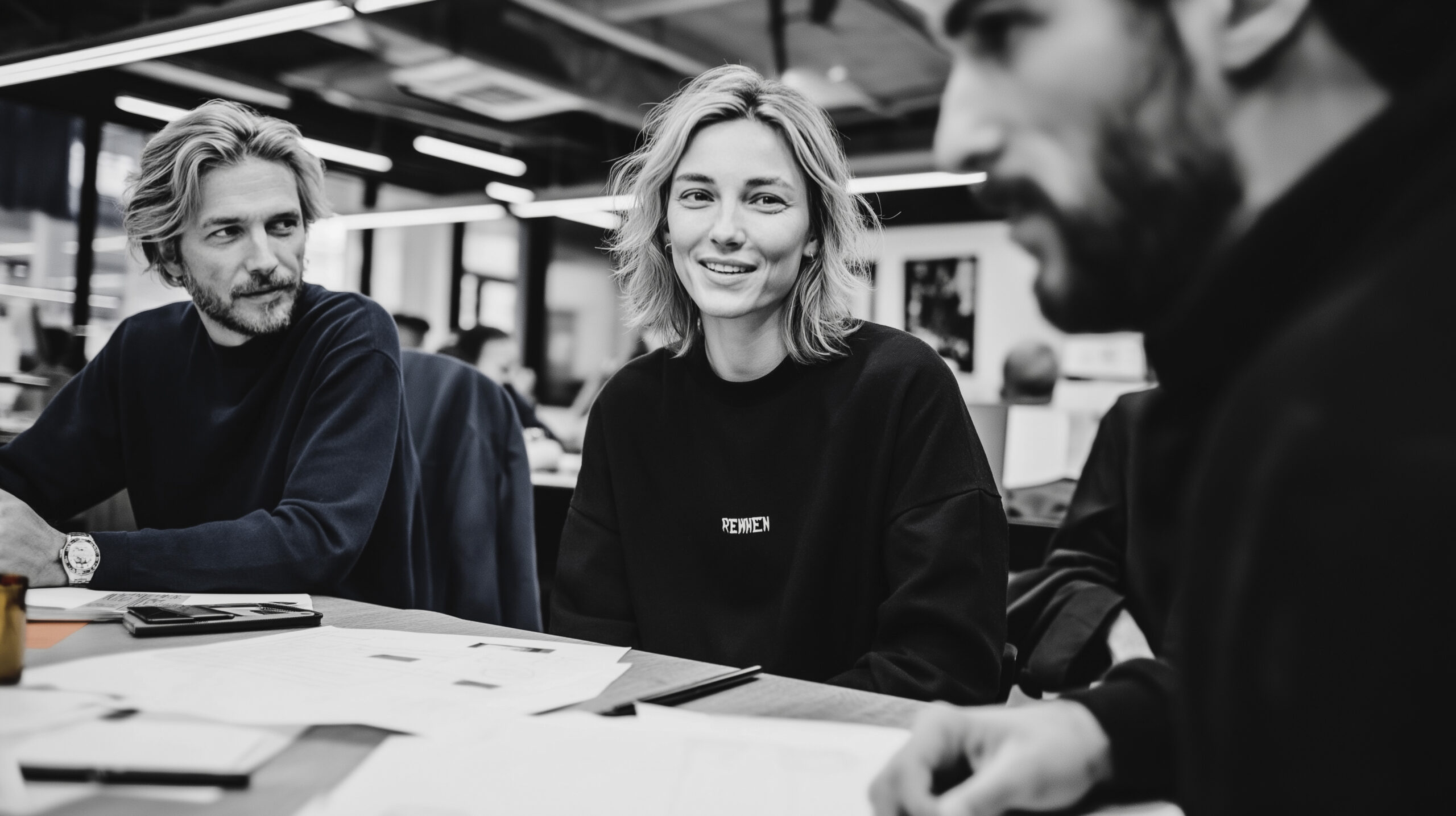 Black and white editorial image of coworkers discussing ideas around a table, capturing real workplace interaction.